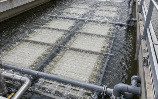 Industrial membrane bioreactor MBR wastewater treatment basin with submerged membrane racks, fine bubble aeration, permeate piping, and engineers inspecting the system