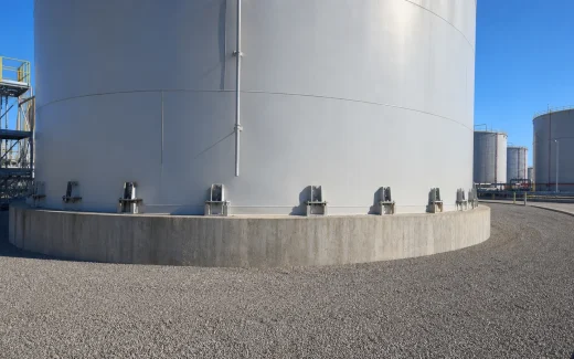 Large above-ground steel storage tank on a reinforced concrete ringwall with accessible anchor chairs and anchor bolts around the shell perimeter
