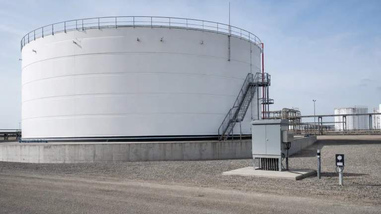Above-ground steel storage tank on a concrete ringwall with cathodic protection test stations and foundation interface visible at an industrial tank terminal